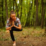 A woman meditates in a yoga pose amidst tranquil woods, focused on relaxation.